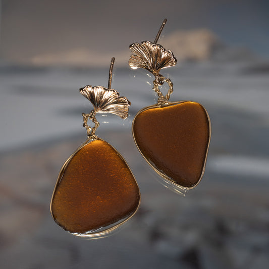 Handmade sea glass earrings featuring warm amber with gold wire.  photographed against a misty beach sunset background.