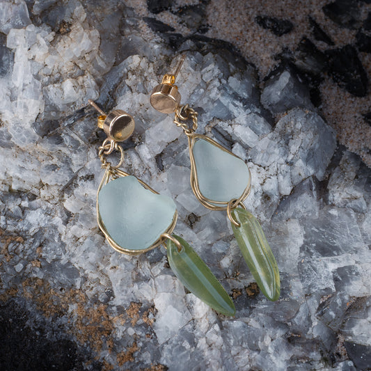 Handmade sea glass necklace featuring cool Ice like glass and soft green glass pieces on a gold chain, photographed against a misty beach sunset background. Hypoallergenic 