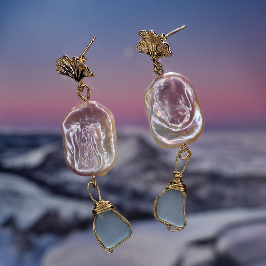 Cyan Seaglass wrapped in gold wire and pink keshi pearl with hypoallergenic stud earrings photographed on blurry sunset pink beach background 